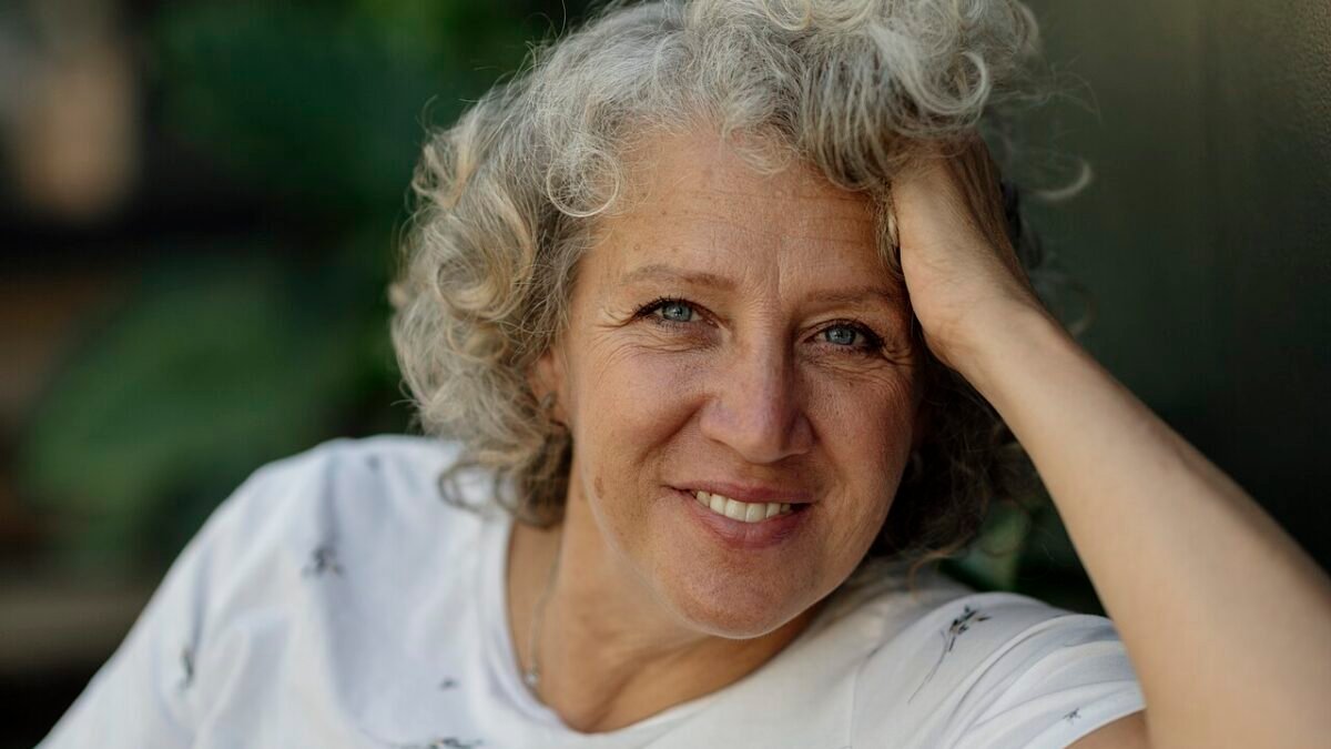 Femme aux cheveux bouclés gris souriant, main dans les cheveux