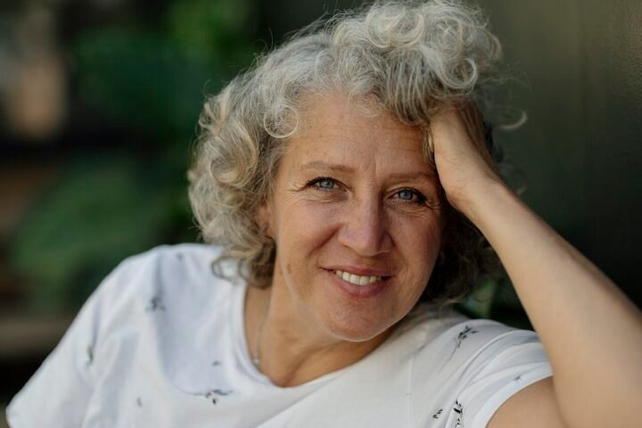 Femme aux cheveux bouclés gris souriant, main dans les cheveux