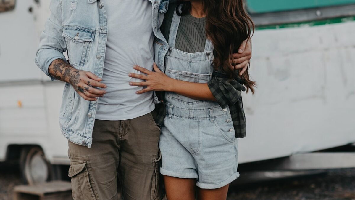 Jeune couple marchant main dans la main, souriant, devant une caravane