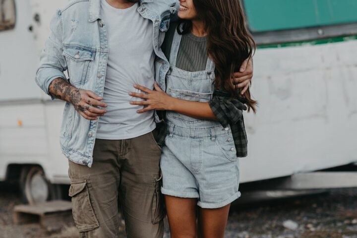 Jeune couple marchant main dans la main, souriant, devant une caravane