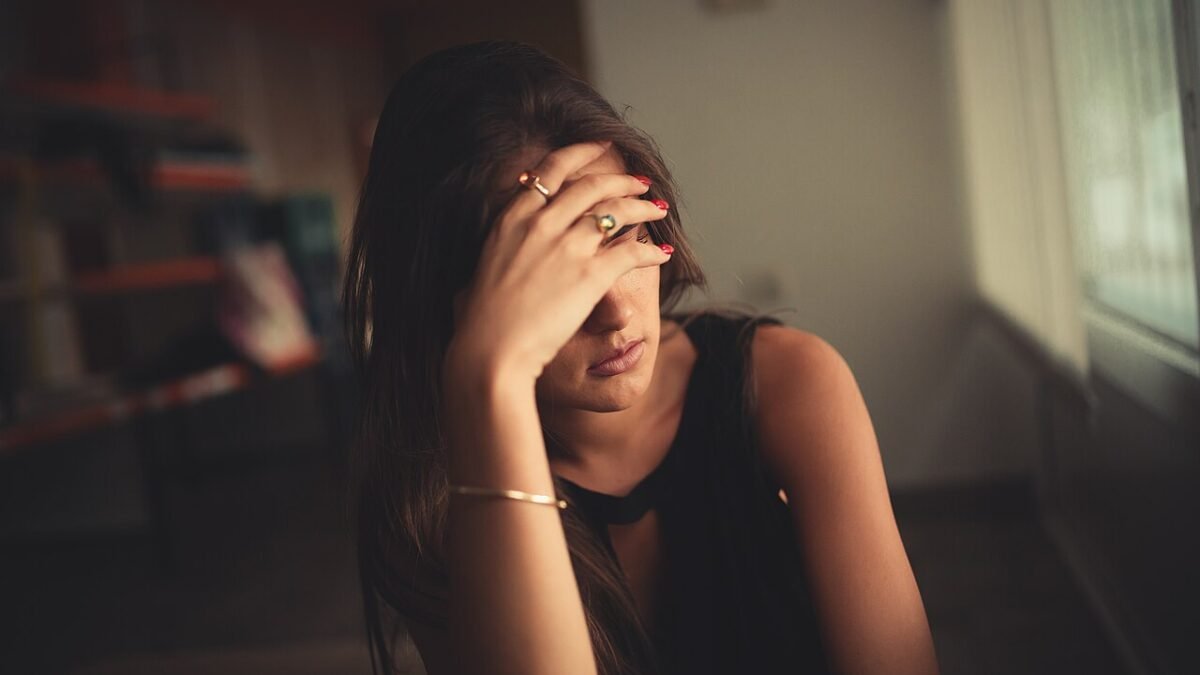 Jeune femme assise, une main devant le visage, dans une pièce sombre