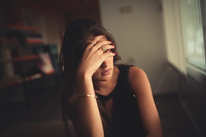 Jeune femme assise, une main devant le visage, dans une pièce sombre