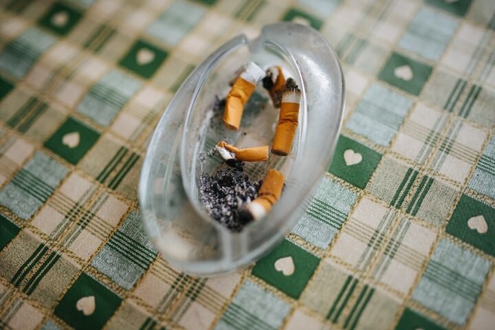 Cendrier en verre rempli de mégots sur une nappe à carreaux