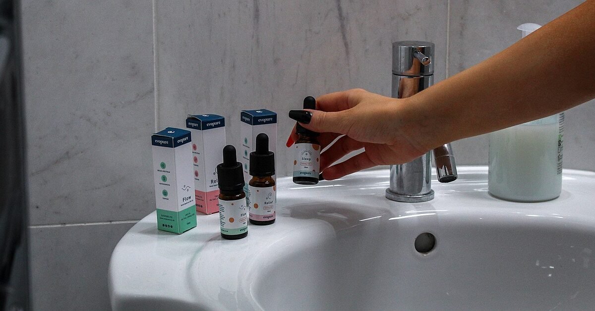 Main attrapant un flacon d'huile de CBD sur le bord d'un lavabo