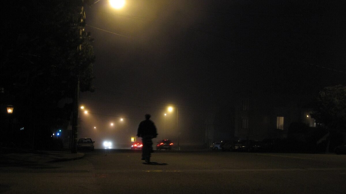 Rue déserte la nuit, sous un lampadaire, silhouette au loin