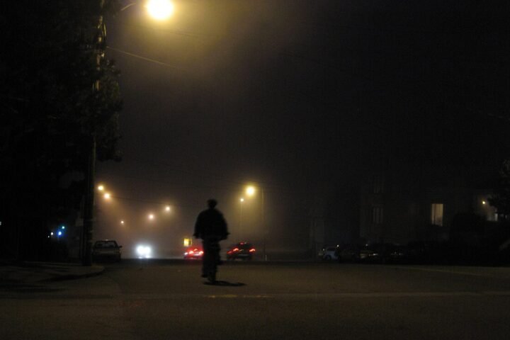 Rue déserte la nuit, sous un lampadaire, silhouette au loin