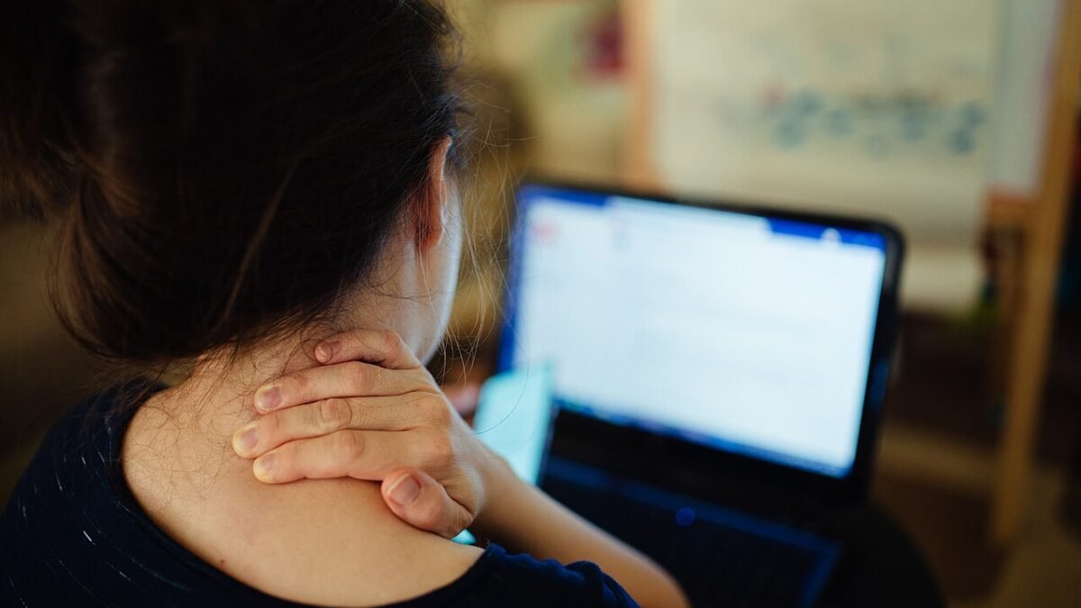 Femme de dos devant un ordinateur portable, main sur la nuque