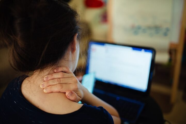 Femme de dos devant un ordinateur portable, main sur la nuque