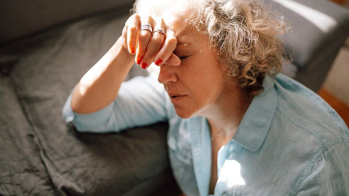 Femme allongée sur un canapé, main sur le front, l'air tendu