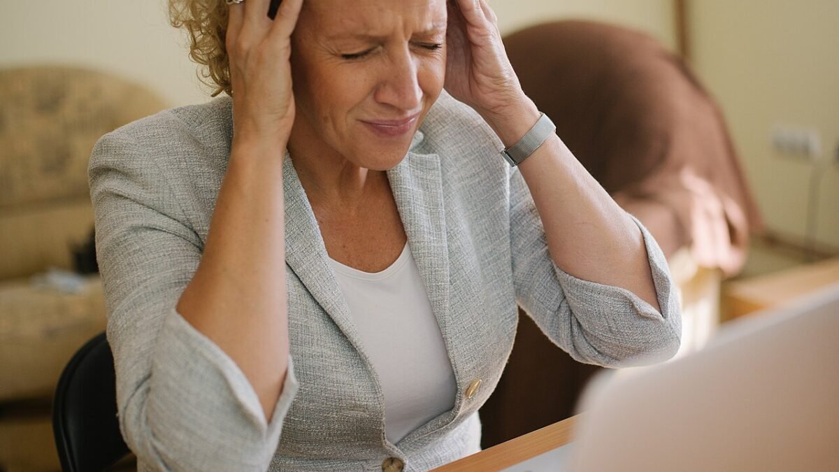 Femme à son bureau devant un ordinateur portable, mains sur les tempes