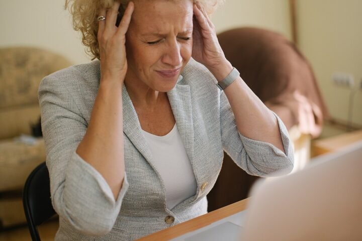 Femme à son bureau devant un ordinateur portable, mains sur les tempes