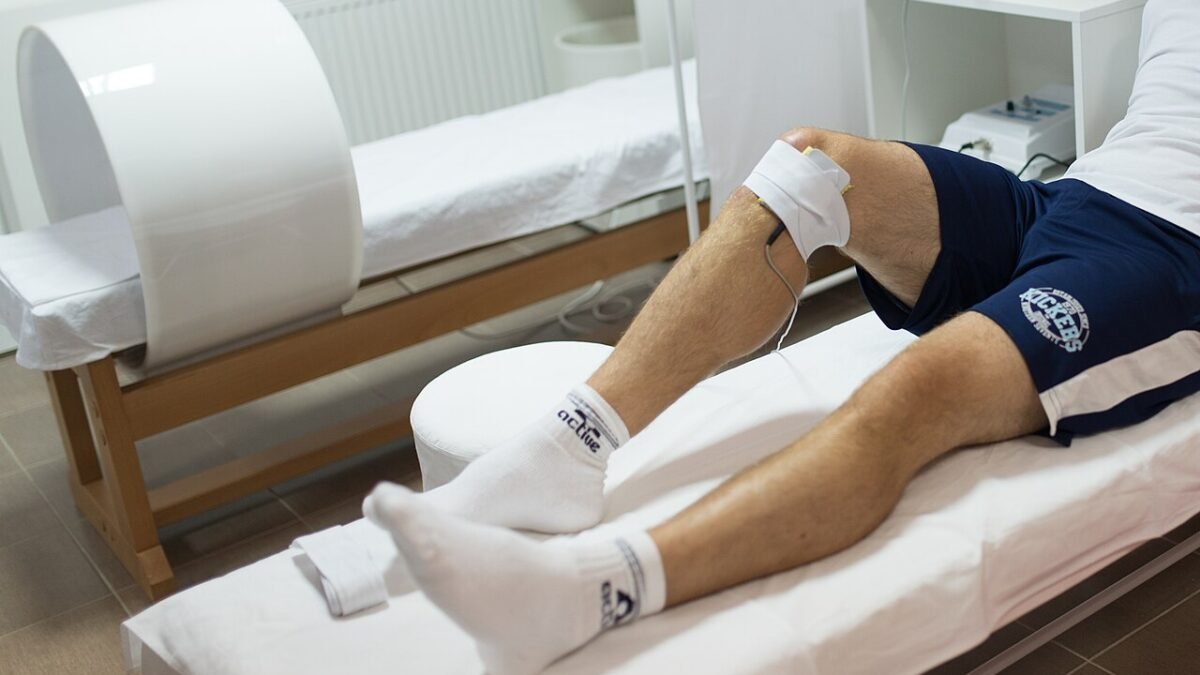 Athlète allongé sur une table de soins, jambe traitée par un praticien