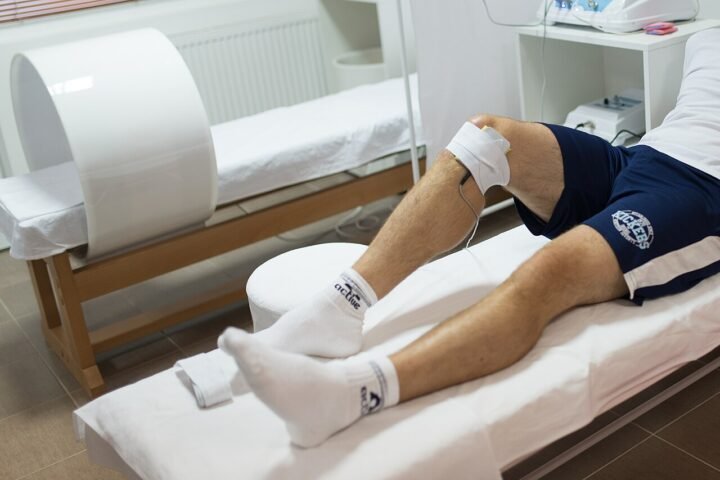 Athlète allongé sur une table de soins, jambe traitée par un praticien