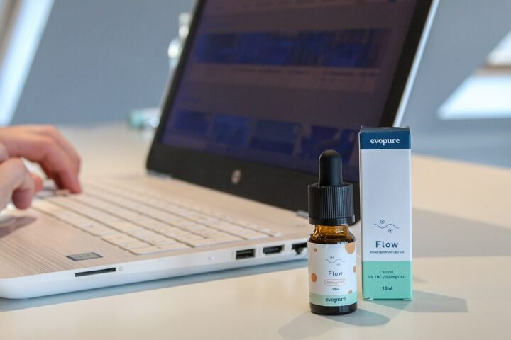 Flacon d'huile de CBD posé sur un bureau à côté d'un ordinateur portable