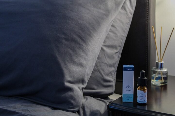 Flacon d'huile de CBD sur une table de chevet, lit en arrière-plan