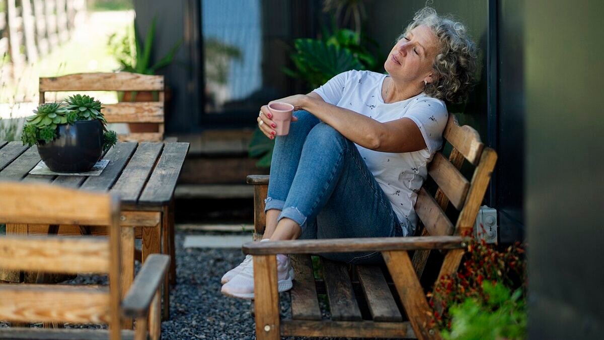 Femme aux cheveux gris assise sur un banc en bois avec une tasse, détendue