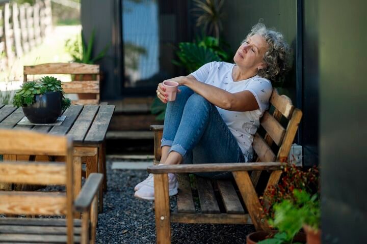 Femme aux cheveux gris assise sur un banc en bois avec une tasse, détendue